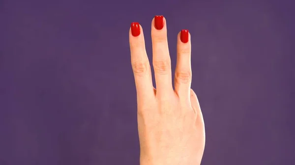 Female hand counting from 3 on purple background. Girl shows three fingers. High quality photo