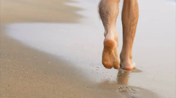 Mens feet walk along the shore line, leaving footprints. High quality photo