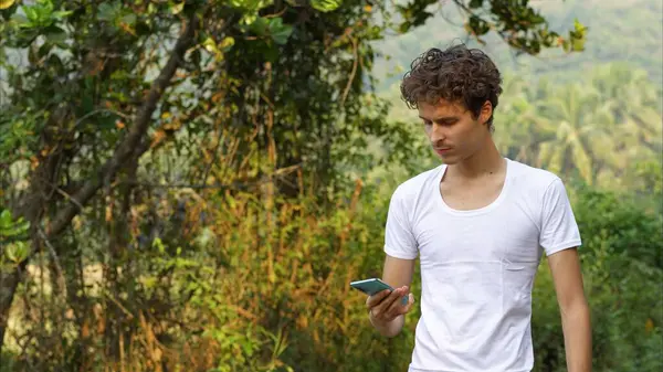 man walking with phone in his hands on the background of green tropical trees