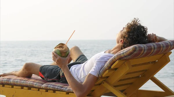 Office worker on a sunbed by the sea drinks coconut. High quality photo