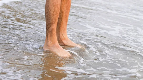 Male feet in sea water on the beach. High quality photo