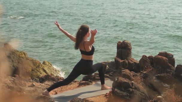年轻女子正在海滨岩石海岸上做Ashva Sanchalanasana 高质量的4K镜头 — 图库视频影像