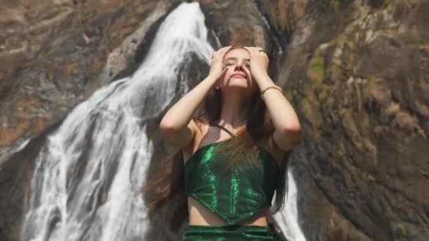 トロピカルジャングルの滝にポーズする緑のドレスの長い髪の女性 高品質の4K映像 — ストック動画