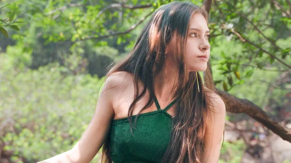young woman looks sideways in a green swimsuit against the background of a park. High quality photo