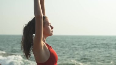 Genç kadın ellerini gökyüzüne kaldırdı ve okyanusun kokusunu içine çekiyor. Yüksek kalite 4k video kaydı