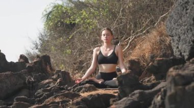 Kadın, doğadaki kayaların üzerinde lotus pozisyonunda oturur. Yüksek kalite 4k video kaydı