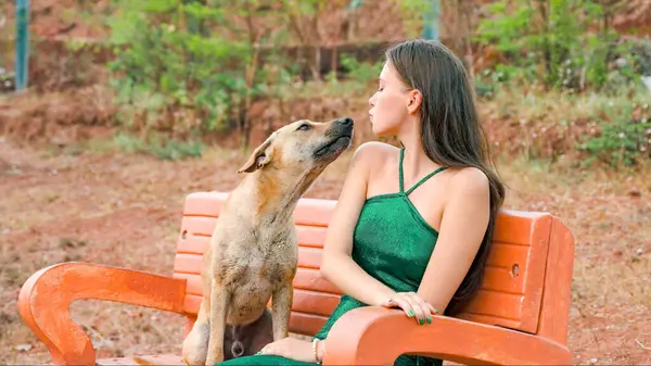 young woman blowing a kiss to a homeless dog on a bench in a tropical park. High quality photo