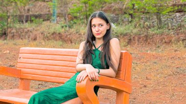 Genç bir kadın parkta bir bankta otururken şaşırtıcı bir şekilde yana bakıyor. Yüksek kalite fotoğraf