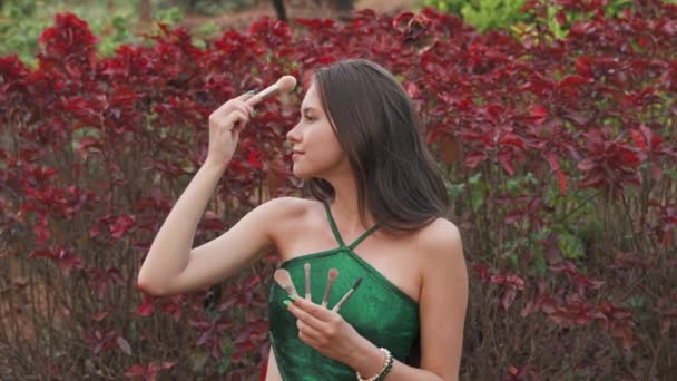 Jovem Segurando Pincéis Maquiagem Contra Fundo Flores Vermelhas Imagens Vídeo — Vídeo de Stock