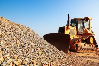 it is construction caterpillar tractor working with pile of gravel and sky.
