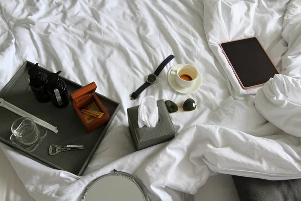 stock image Top view of tablet, watch, black glasses, cup of coffee, gray box of napkin, bottle opener, wooden box and plastic conditioner shampoo and bath shower gel on white blanket with copy space. Object