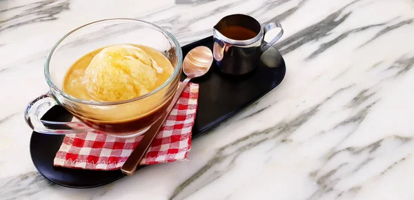 Affogato coffee dessert, Cup of vanilla ice cream with espresso and tea spoon putting on red plaid cotton with stainless mug shot in black tray on white marble table with copy space- Refreshment drink
