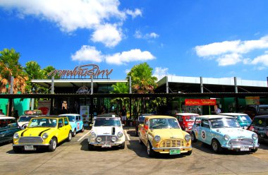 Nakhonratchasima, Thailand - January 31, 2023: Colorful classic Mini Austin cooper parking on street in front of Thai coffee shop with building and blue sky background. Small vehicle, Vintage car 