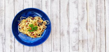 Flat lay or top view spaghetti with clams and mushroom sliced or Italian seafood pasta and parsley on top food in blue dish on white grunge or rough wooden background or table with right copy space 