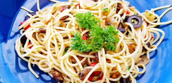 Close up hot spicy spaghetti with clams and mushroom sliced or Italian seafood pasta and parsley or green herb on top in blue dish.