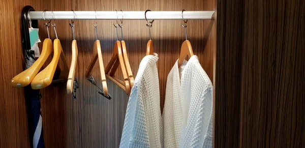 Two white clean bathrobes cloth or robe with wooden hanger and hanging inside dark brown closets with light for service customer wearing and taking shower at hotel