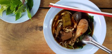 Sıcak tavuklu şehriye, haşlanmış acı kabak, paslanmaz kaşık, mavi kasede kırmızı beyaz çubuklar ve ahşap masada bir sürü sebze tabağı. Asya yemeği ve suyu.