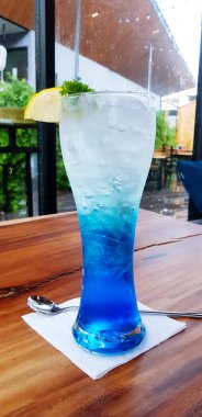 Kahverengi tüp, limon dilimleri ve yeşil yapraklı mavi Hawaii İtalyan soda kokteyli. Ahşap masa üzerinde, kafenin arka planında. Taze içecek ve yaşam tarzı yiyecekler.