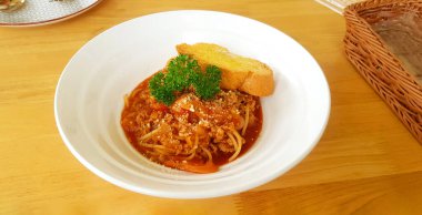 Kıymalı spagetti, tavuk ya da sığır eti, tereyağlı kızarmış ekmek ve ahşap masadaki beyaz tabakta domates sosu. Üzerinde maydanoz olan İtalyan yemekleri ve öğle yemeğinde lezzetli yemekler..