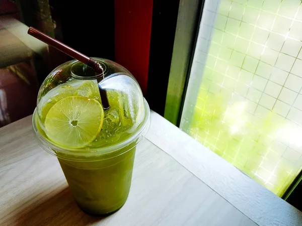 冰凉柠檬绿茶的塑料杯子 桌子上的管子 有复制的空间和阳光从窗口照射在咖啡店 早上再喝两杯 — 图库照片