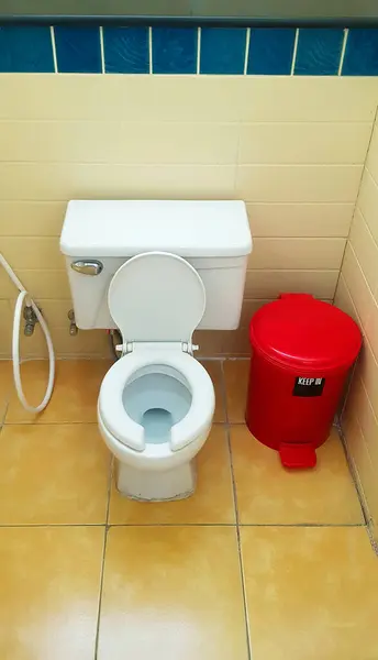 Flush toilet with red trash can on yellow tile in bathroom, restroom. Public washroom and clean room. Design and ceramic object