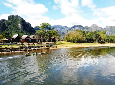Turist uzun kuyruklu tekneye biniyor ve dağlık arazi manzarası, nehir kenarı ve Laos, Vangviang 'da bir sürü ahşap ev görüyor. Gezi, Gezgin ve Yer İmleri konsepti.
