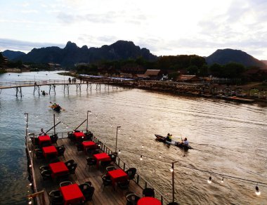 Nehir boyunca uzanan birçok kırmızı restoranın ve masaların ve Luang Prabang, Vang Vieng, Laos 'ta nehirde kürek çeken turistlerin manzarası. Nehir ve dağ manzarası.