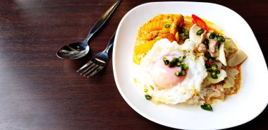 Domuz etli, sebzeli sıcak sarı köri pilavlı kızarmış yumurta, paslanmaz çelik kaşık ve çatal, koyu kahverengi ahşap masa ve fotokopi alanı. Hint yemeği konsepti.