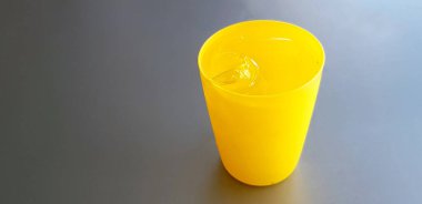 Gri ya da gri arkaplanda izole edilmiş buzla kaplı sarı plastik bardak. Susuzluk, Serinleme ve İçme konsepti 