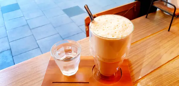 Caramel macchiato frappe with iced water on the wooden table with copy space at cafe shop. Refreshment drinking concept