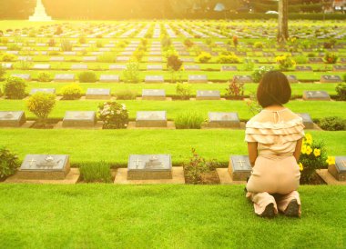Mezarlıkta siyah mezar taşının önünde oturan Asyalı kadın. Eski günleri yâd et, bayan, üzül ve ailede birini kaybet ya da önemli birini ya da insanları..