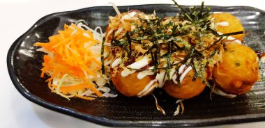 Japon restoranında Takoyaki 'yi havuç, lahana dilimi ve siyah tabakta kurutulmuş yosun ile kapatın. Kızarmış ve Asya yemekleri.   