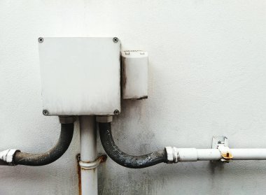 Kopya alanı olan beyaz beton duvara bağlı kablolar için bağlantı kutusu. Elektrik ya da telefon kablosu, hayvan ısırığı kablosunu korumak için boruya bağlanır. Kablolama ve sistem.