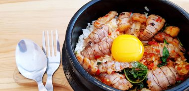 Kızarmış Tayland fesleğenini kerevit ve yumurta sarısını paslanmaz çelik kaşıkla sıcak siyah klozete koy ve ahşap masada müşterilere servis yapmak ve yemek yemek için hazır hale getir. Baharatlı yemekler ve Asya yemekleri..