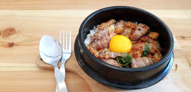 Kızarmış Tayland fesleğenini kerevit ve yumurta sarısını paslanmaz çelik kaşıkla sıcak siyah kasede ve ahşap masada müşteriye servis yapmak ve yemek için insanları karıştırın. Baharatlı yemekler ve Asya yemekleri..