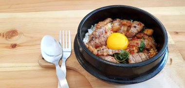 Kızarmış Tayland fesleğenini kerevit ve yumurta sarısını paslanmaz çelik kaşıkla sıcak siyah kasede ve ahşap masada müşteriye servis yapmak ve yemek için insanları karıştırın. Baharatlı yemekler ve Asya yemekleri..