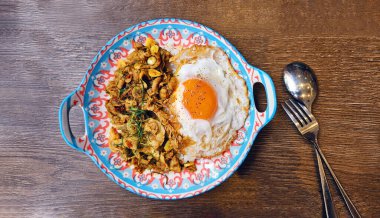 Tayland usulü sahanda yumurta ve çatalla ahşap zemin üzerinde kaşık eşliğinde pirinçle karıştırılmış sığır eti, domuz ya da tavuk. Tayland 'da kahverengi masada baharatlı ve ünlü yiyecekler..