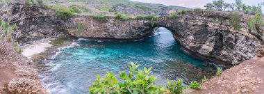 Kırık sahildeki doğal köprünün geniş manzaralı bir fotoğrafı. Güzel gel-git havuzlu ve nefes kesici doğa manzaralı bir turistik mekan. Nusa Penida Adası, Endonezya