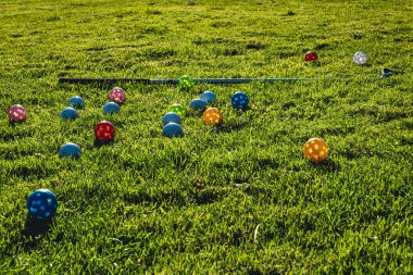 Birçok açık renkli plastik golf topu ve yeşil çimlerde bir golf sopası. Evde golf antrenmanı yapıyorum.