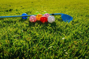 Birçok açık renkli plastik golf topları, delikli ve bir golf sopası yeşil çimlerde yan yana yatar. Evde golf antrenmanı yapıyorum. Düşük seviye fotoğraf