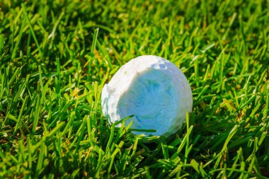 Kırık bir beyaz golf topu yeşil çimlerin üzerinde yatıyor. Hasarlı golf topu, fotoğrafı kapat.