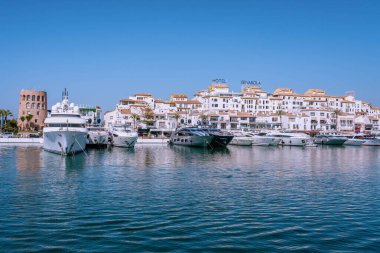 Beyaz lüks yatlar ve botlar Porto Banus limanında demirlemiş, arka planda beyaz binalar ve palmiye ağaçları, Marbella, İspanya
