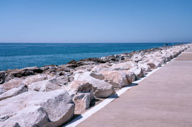 Güneşli bir günde asfalt kaldırımla mavi okyanusu birbirinden ayıran taştan dalgalı su.