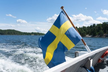 İsveç bayrağı dalgalanır yelkenli Stockholm takımadalarından güneşli yaz gününde, mavi gökyüzü ve bulutlar, yeşil adalar, özgürlük ve seyahat konsepti