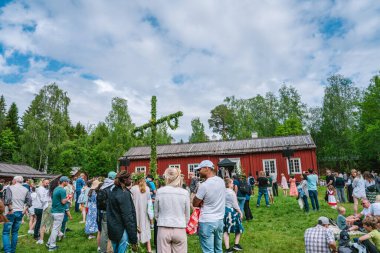 Turistler yaz dönümünü Gammlia, Umea, İsveç 'teki geleneksel kırmızı ahşap bir evin önünde kutluyorlar ve güneşli bir günün tadını çıkarıyorlar. UMEA, GAMLIA, İSVEÇ 23 HAZİRAN 2023