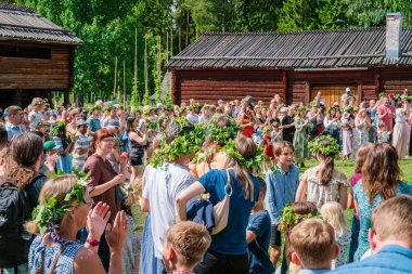 Turistler ve yerliler Gammlia, Umea, İsveç 'te yaz dönümünü dans ederken ve alkışlarken çiçek çelenkleri giyerek kutluyorlar. UMEA, GAMLIA, İSVEÇ 23 HAZİRAN 2023