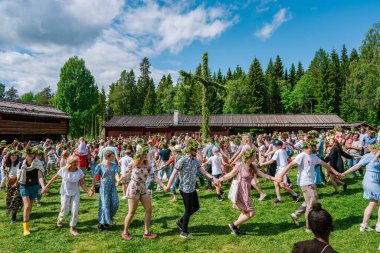 Gammlia, Umea, İsveç 'te düzenlenen güneşli yaz kutlamalarında turistler ve yerliler meyhane direğinin etrafında el ele dans ediyorlar. UMEA, GAMLIA, İSVEÇ 23 HAZİRAN 2023