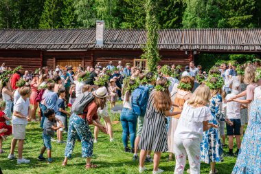 İsveç 'in Umea, Gammlia şehrinde düzenlenen bir yaz kutlaması sırasında, turistler ve yerliler çiçek çelenkleriyle meydanda dans ediyorlar. UMEA, GAMLIA, İSVEÇ 23 HAZİRAN 2023