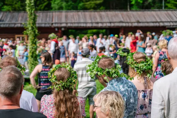 Çiçekli çelenk giyen turistler ve yerliler, geleneksel bir ahşap binanın önünde, İsveç 'in Gammlia kentinde düzenlenen bir yaz dönümü kutlamasına katılıyorlar. UMEA, GAMLIA, İSVEÇ 23 HAZİRAN 2023