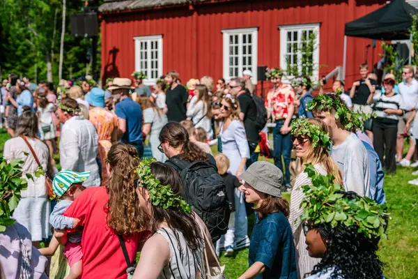 Çiçekli çelenk giyen turistler ve yerliler Gammlia, Umea, İsveç 'te toplanarak yaz dönümünü kutluyor ve meyhane direğinin etrafında dans ediyorlar. UMEA, GAMLIA, İSVEÇ 23 HAZİRAN 2023